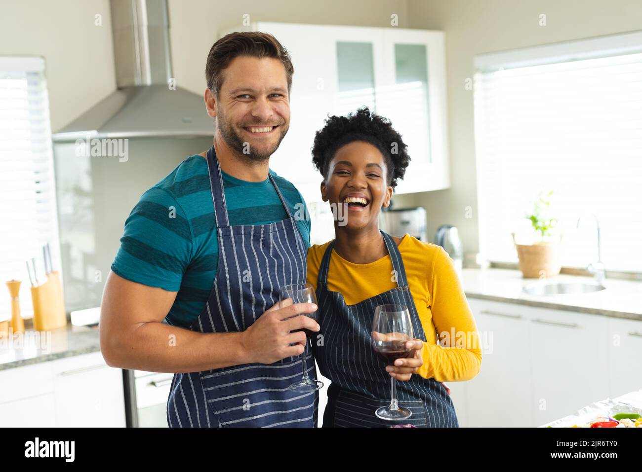 Immagine di felice coppia varia in grembiuli con vino in cucina Foto Stock