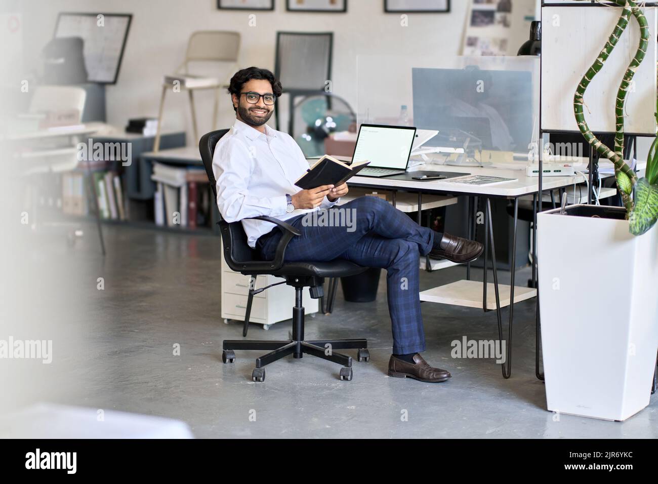 Felice uomo indiano di affari che tiene l'organizzatore seduto al lavoro in ufficio. Foto Stock