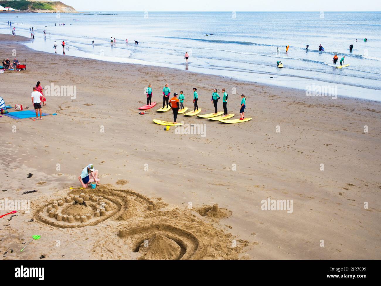 Istruttori e studenti imparano a fare surf nella baia nord di Scarborough con elaborati castelli di sabbia in primo piano Foto Stock