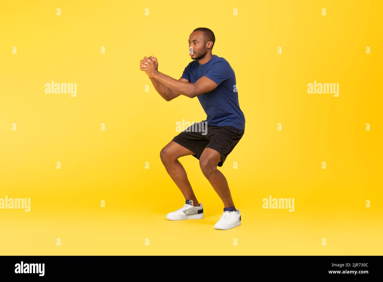 Atletico Africano americano uomo che fa profondo squat esercizio, sfondo giallo Foto Stock