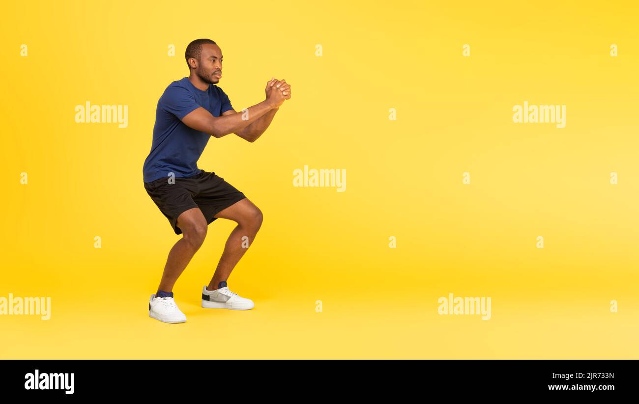 Sportivo Black Guy allenarsi facendo squat profondi su sfondo giallo Foto Stock