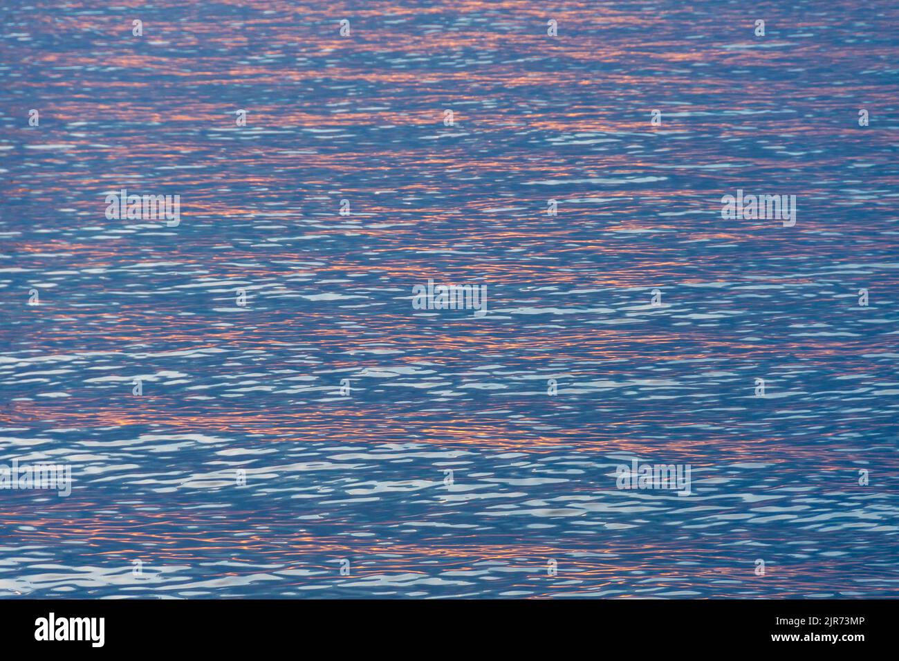 Riflessi rossi del sole che sorge all'alba nelle calme acque del Mar Mediterraneo. Texture e sfondo per vacanze, riposo e concetti di serenità Foto Stock