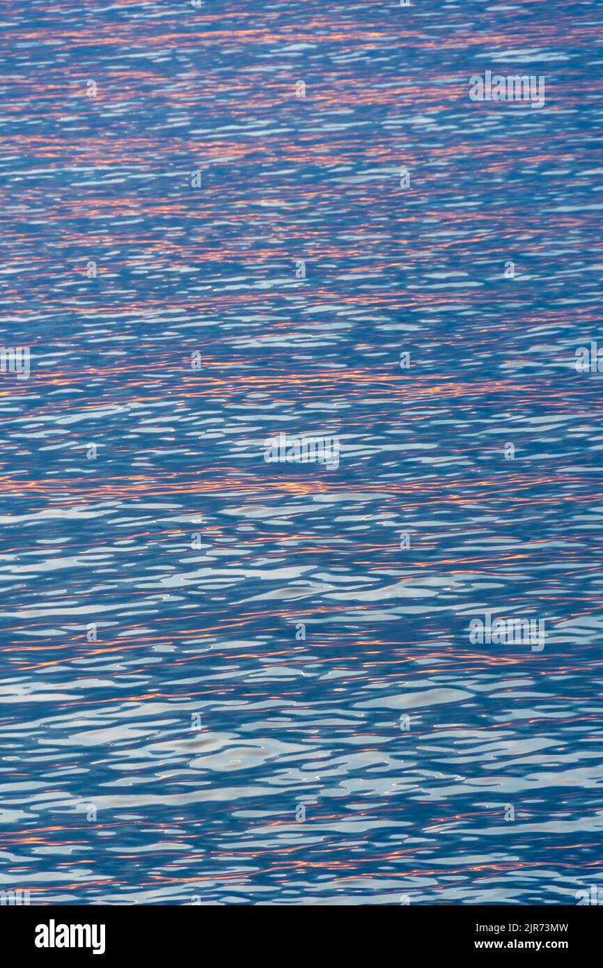 Riflessi rossi del sole che sorge all'alba nelle calme acque del Mar Mediterraneo. Texture e sfondo per vacanze, riposo e concetti di serenità Foto Stock