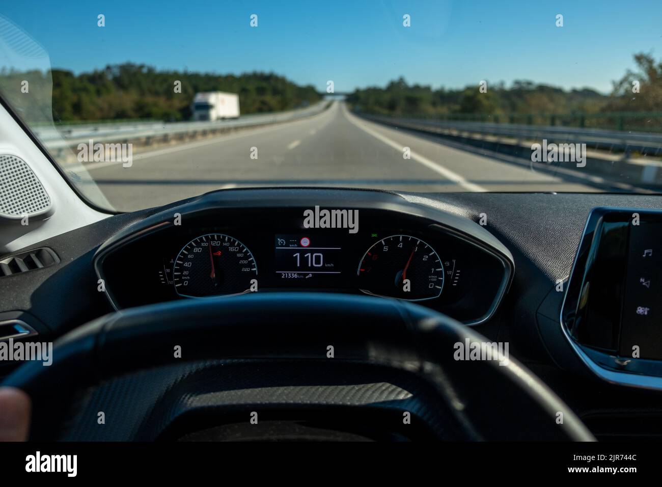 Vista del conducente sul tachimetro a at110 km/h o 110 mph e la strada sfocata in movimento, vista dall'interno di un'auto del conducente POV del paesaggio stradale. Foto Stock