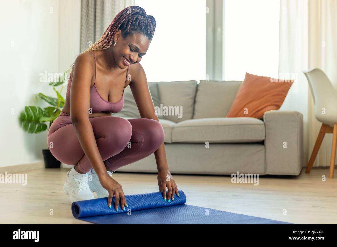 Concetto Stay FIT. Giovane donna afroamericana in abbigliamento sportivo tappeto yoga rolling dopo l'esercizio a casa Foto Stock