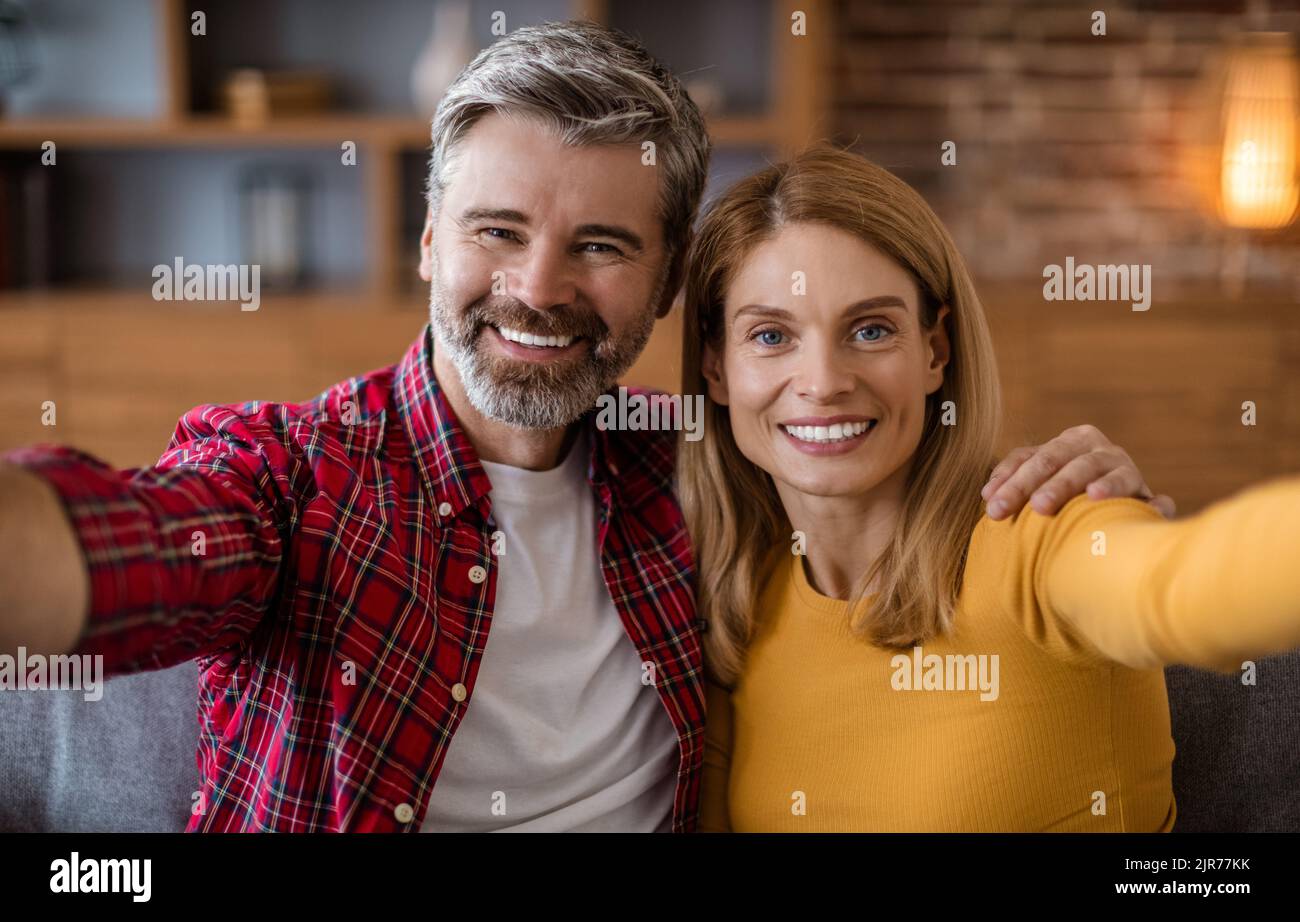 Allegro caucasico di mezza età maschio e femmina guardare la macchina fotografica, divertirsi, fare foto nel salotto interno Foto Stock