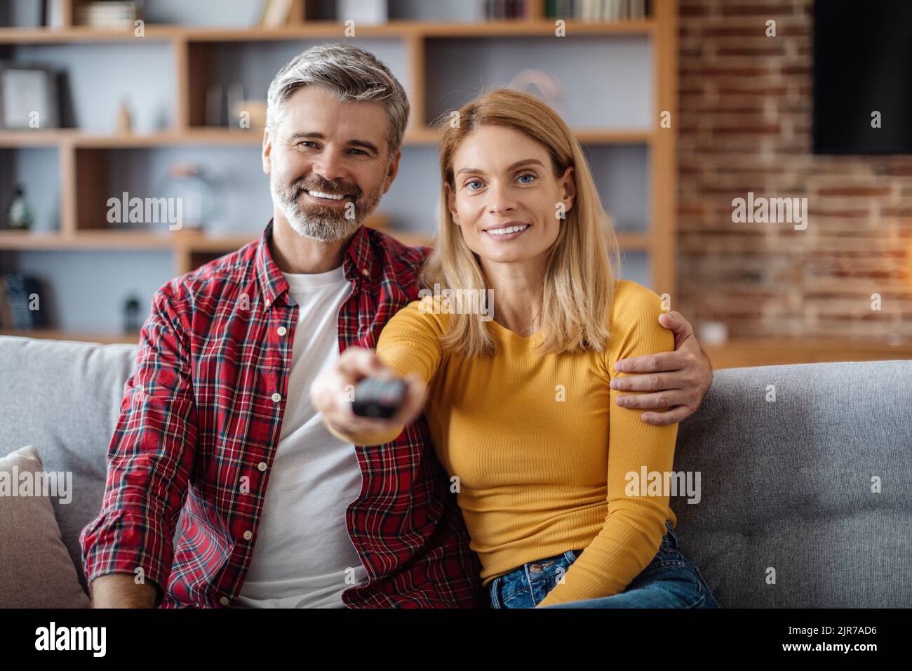 Allegra donna caucasica di mezza età con telecomando e l'uomo godere della partita a tempo libero, guardare la tv Foto Stock