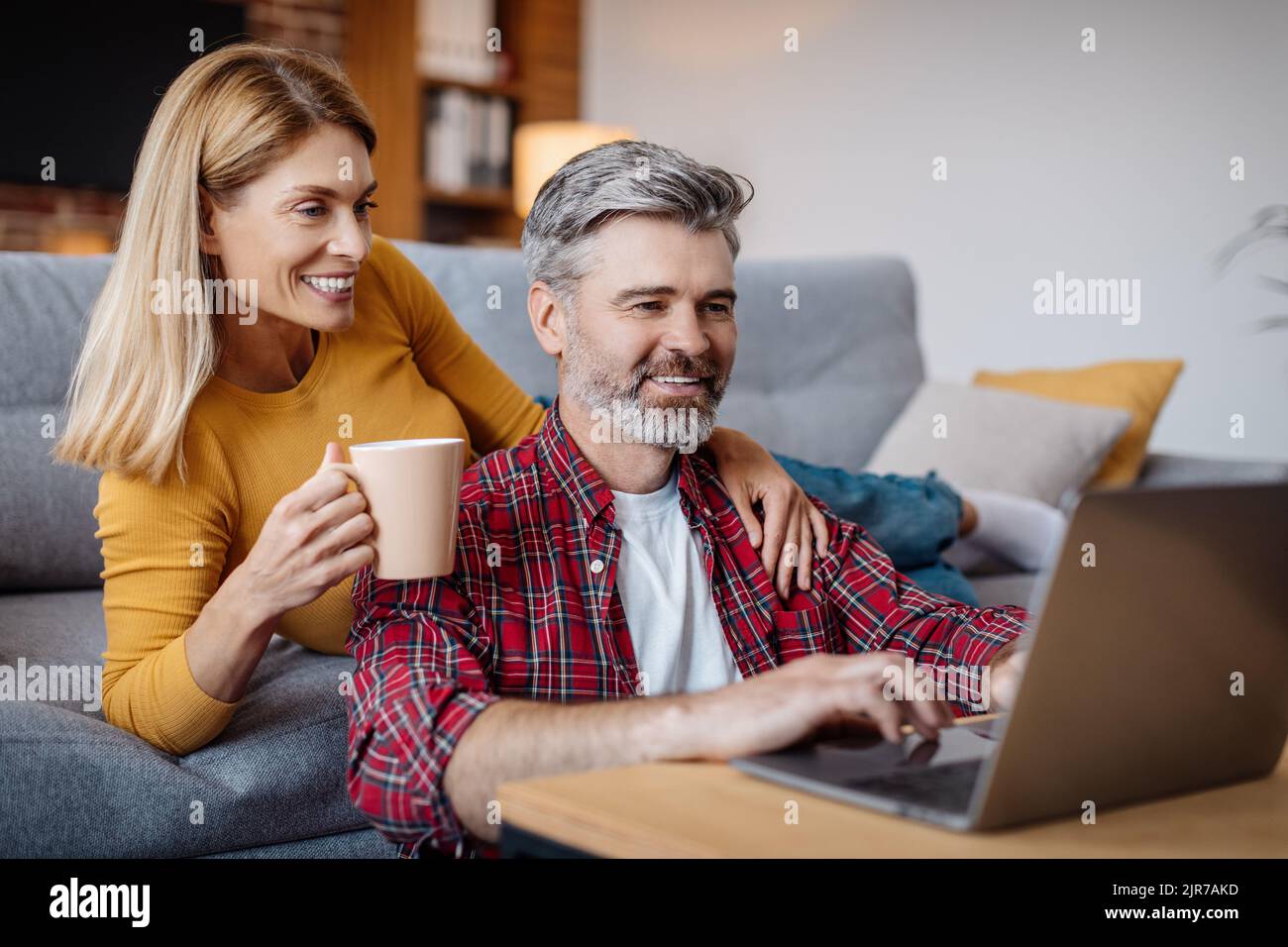 Felice moglie e marito caucasico maturo guardando il computer portatile, goditi una pausa caffè nel tempo libero nel soggiorno Foto Stock