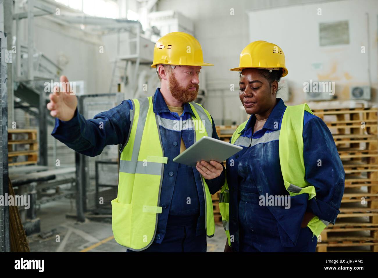 Giovane ingegnere maschile fiducioso in abbigliamento da lavoro e hardHat che spiega i momenti tecnici di un nuovo progetto alla riunione Foto Stock