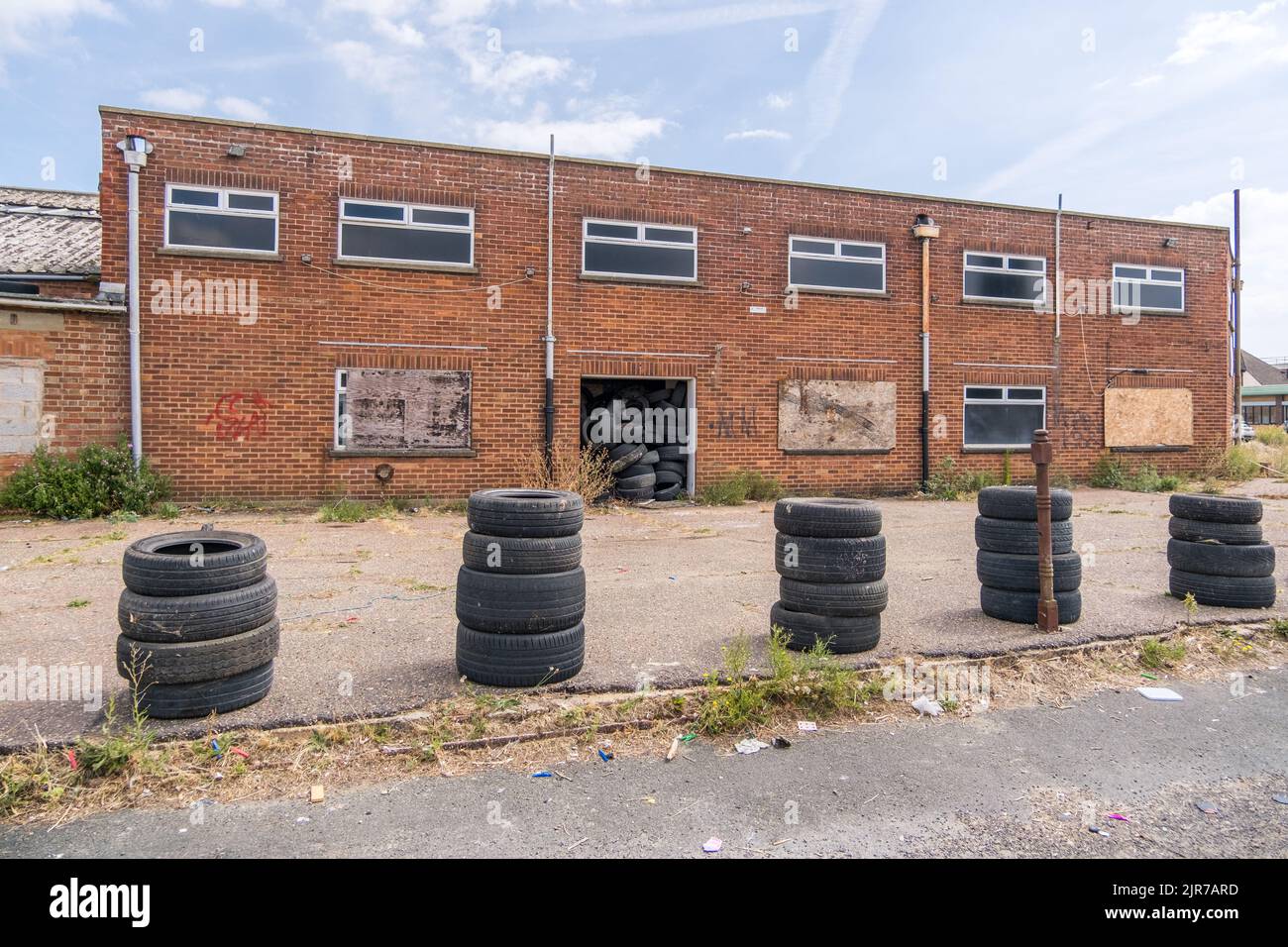 Pneumatici auto impilati di fronte a un edificio abbandonato in una zona industriale, zona portuale di Great Yarmouth, Norfolk, Inghilterra. Foto Stock