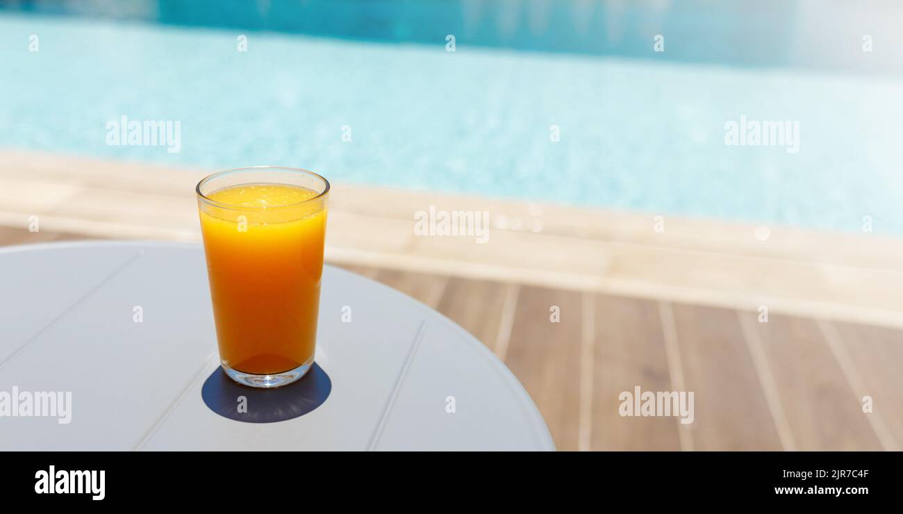 Bicchiere di fresco succo d'arancia drink sul tavolo accanto alla piscina, vacanza tropicale estiva concetto. Banner con spazio di copia Foto Stock