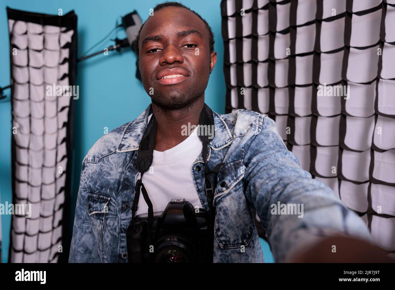 Sicuro direttore dello studio di produzione che scatta foto selfie mentre si trova accanto a un'attrezzatura di ripresa professionale. Un appassionato di fotografia che fotografa se stesso accanto a softbox e faretti. Foto Stock