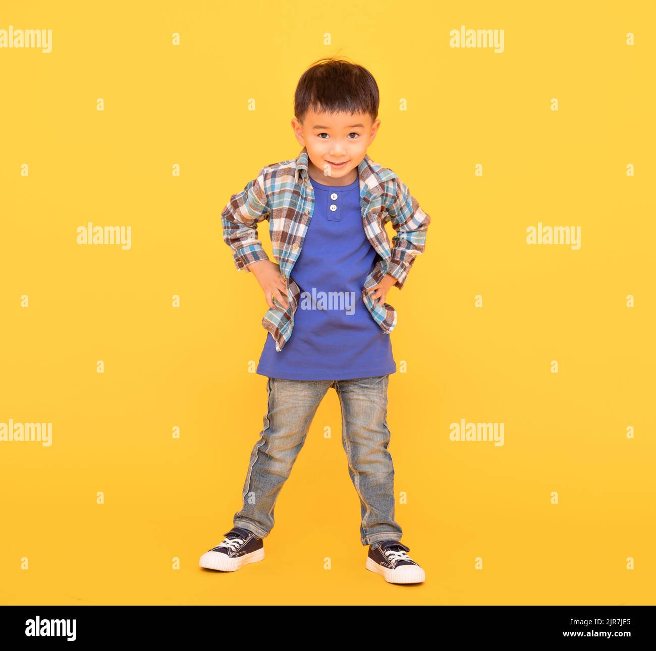 felice ragazzo asiatico in piedi su sfondo giallo Foto Stock