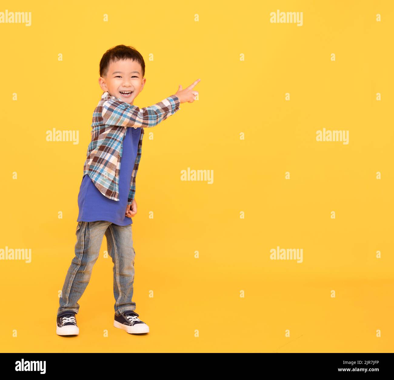 felice ragazzo asiatico in piedi e puntando su sfondo giallo Foto Stock