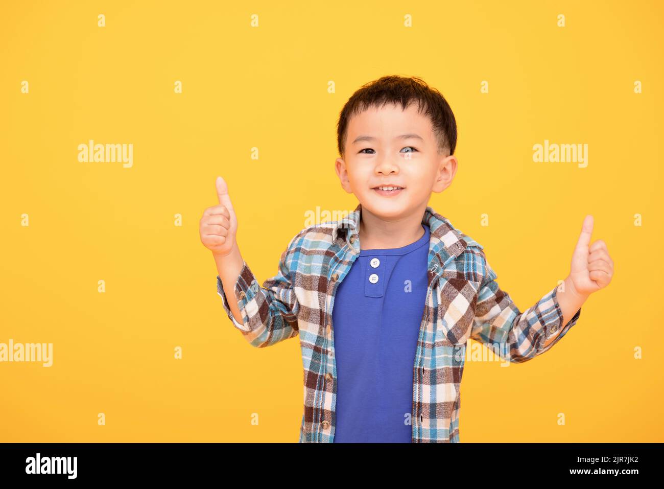 ragazzo felice di fronte a sfondo giallo e mostrando pollici in su Foto Stock