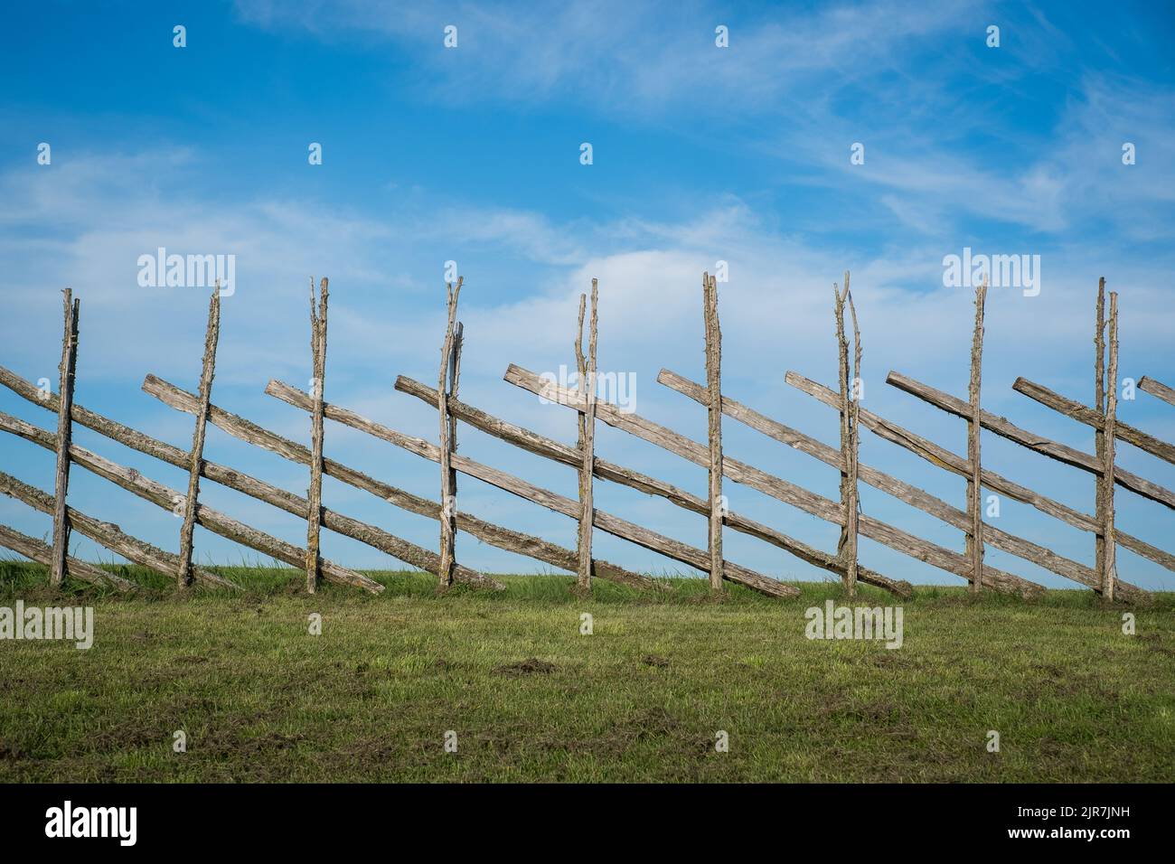 Antica recinzione in legno fatta a mano con erba verde e cielo blu. Estate sfondo di stile country. Foto Stock