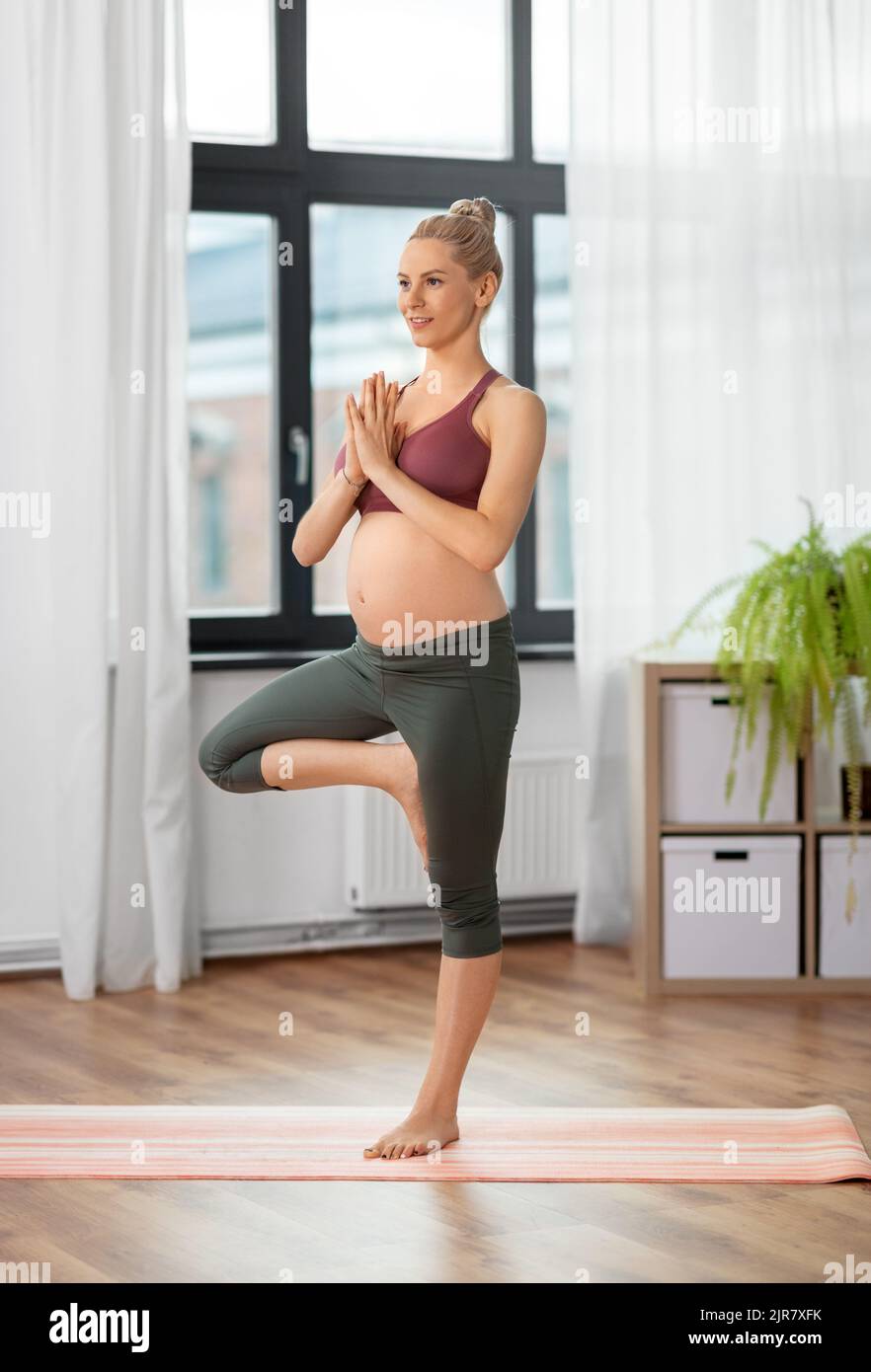donna incinta felice che fa yoga a casa Foto Stock