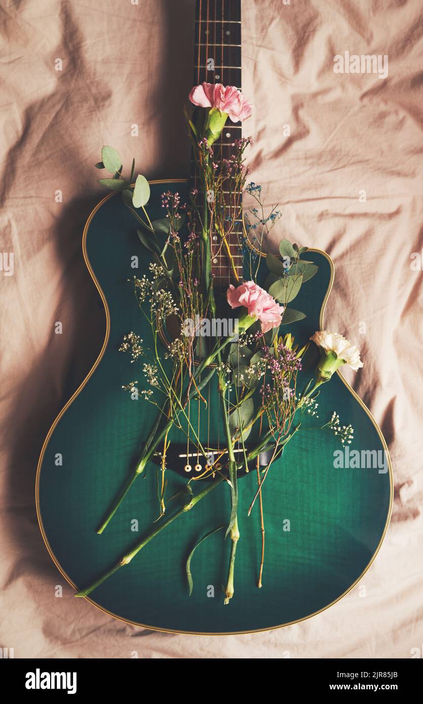 La musica fa crescere i tuoi pensieri. Ripresa ad angolo alto di una chitarra verde sdraiata su un letto con fiori disposti su di esso. Foto Stock