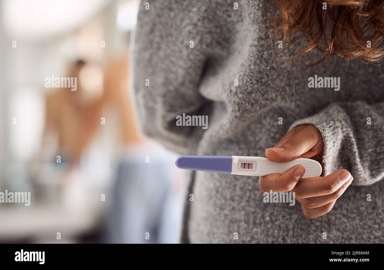 Questo potrebbe cambiare tutto. Una donna irriconoscibile che nasconde un test di gravidanza dietro la schiena in bagno. Foto Stock