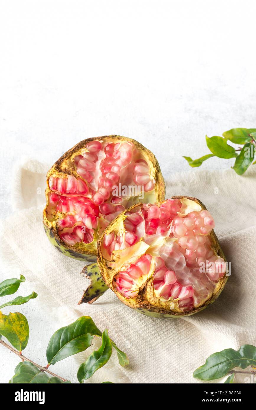 frutto melograno appena raccolto su superficie bianca con le sue foglie, frutto succoso dolce con semi commestibili, preso in fondo morbido-fuoco Foto Stock