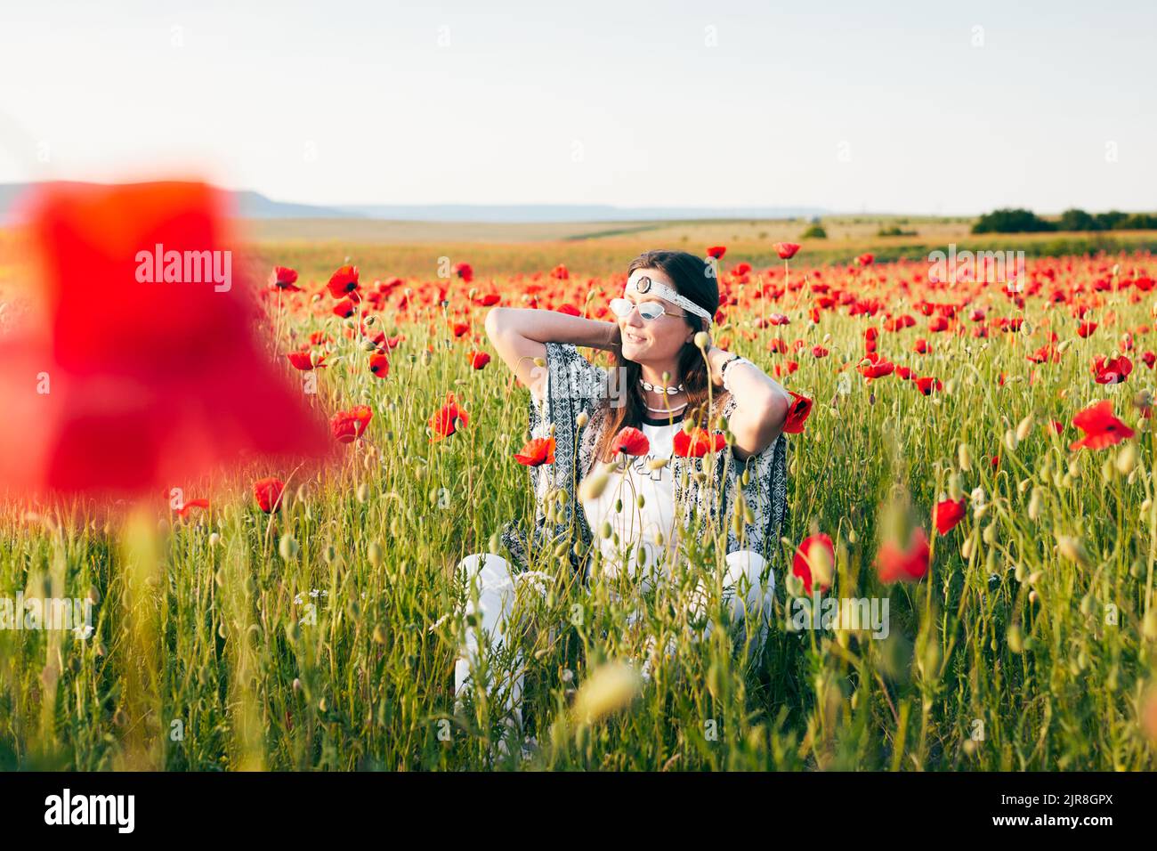 Una giovane donna si pone in un campo con papaveri selvatici rossi al tramonto. Vista frontale. Foto Stock
