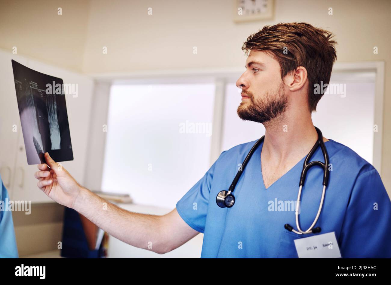 HES cercando di capire una diagnosi. Un giovane medico che analizza una radiografia da solo nel suo ufficio. Foto Stock