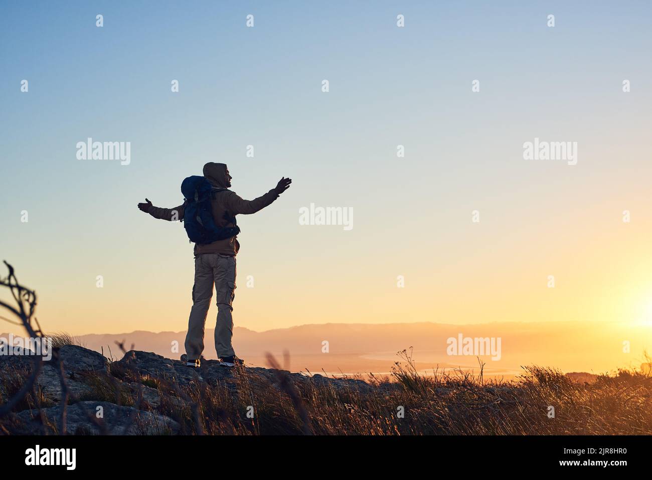 La terra ha musica per coloro che ascoltano: Un escursionista in cima ad una montagna con le braccia alzate la mattina presto. Foto Stock