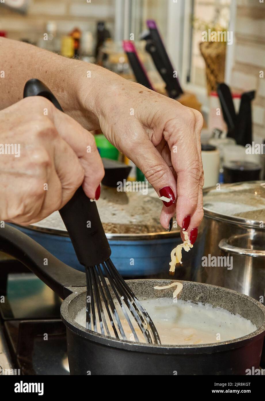 Lo chef lancia il formaggio grattugiato in una pentola di salsa di bechamel, che viene cucinata su una stufa a gas Foto Stock