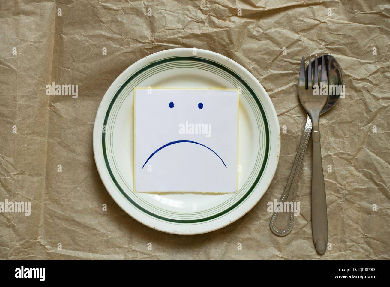 triste udibka disegnato su un pezzo di carta giace su un piatto vuoto sul tavolo, tristezza quando non c'è niente da mangiare, fame e cattivo umore Foto Stock