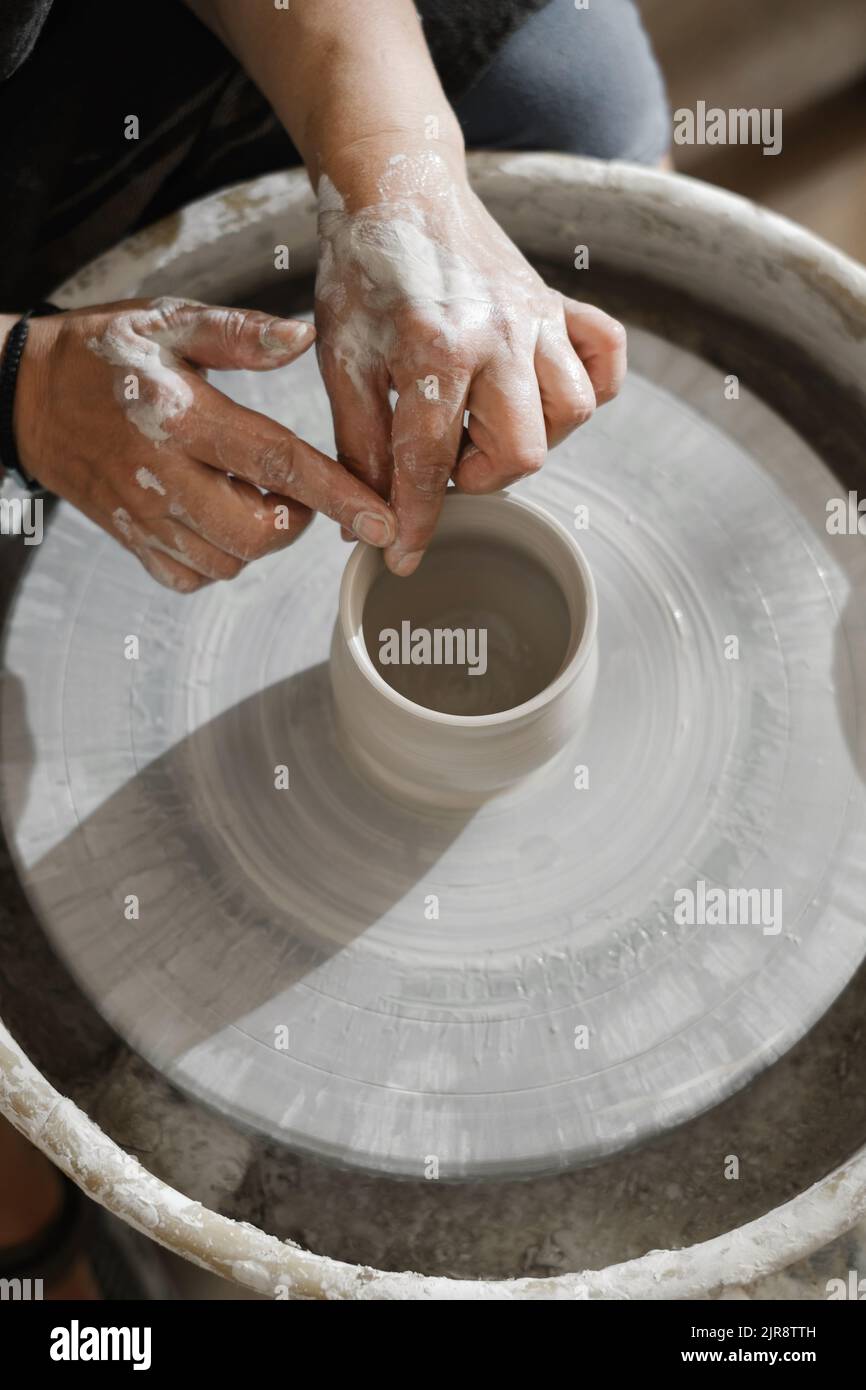 Primo piano delle mani presso un laboratorio di ceramica che impara a fare una ciotola di argilla. Persone che fanno piatti fatti a mano. Lezione per adulti allo studio di ceramica. Vista dall'alto Foto Stock
