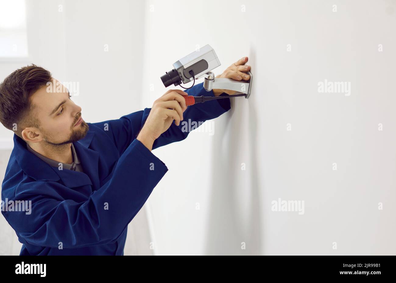 Un tecnico maschile installa una videocamera di videosorveglianza a parete all'interno dell'ufficio per motivi di sicurezza. Foto Stock