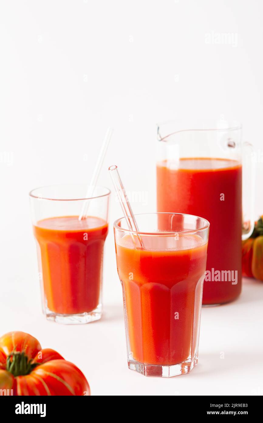 Succo di pomodoro appena spremuto in bicchieri e una caraffa con pomodori su sfondo bianco Foto Stock