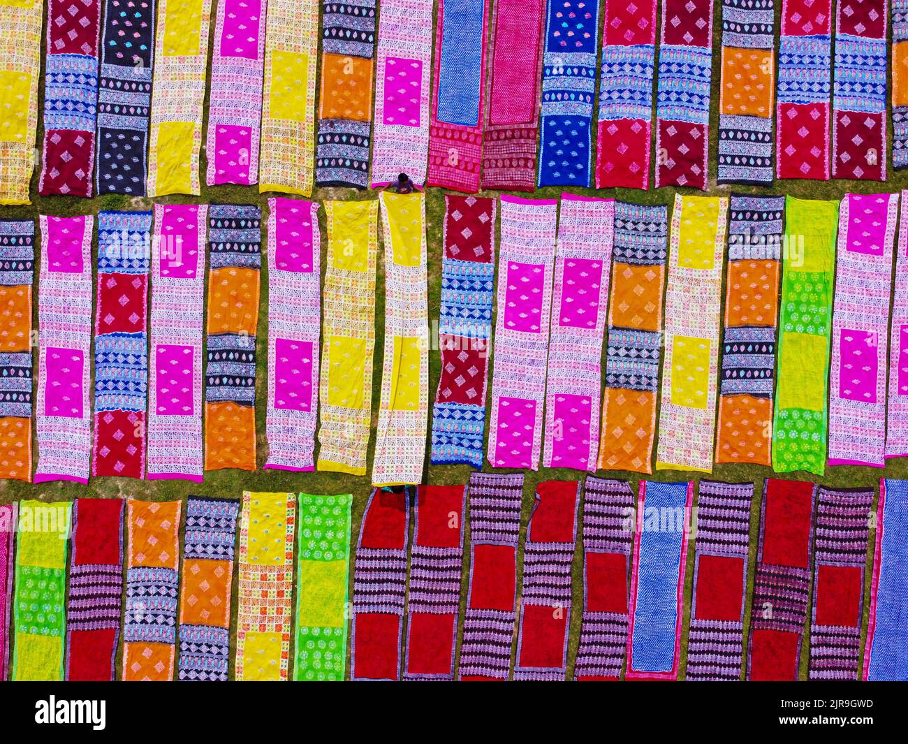 Narayanganj, Dhaka, Bangladesh. 23rd ago, 2022. Strisce colorate di tessuto producono un'esposizione accattivante mentre sono disposte in file ordinate attraverso un campo a Narayanganj, Bangladesh. Localmente chiamato ''Saree'' - un abbigliamento tradizionale per le donne, i lunghi panni di cotone vengono fatti asciugare sotto il sole caldo, essendo stati tinti con colori luminosi. Circa 4000 pezzi di stoffa sono deposti per asciugare qui ogni giorno. Il processo richiede solitamente tre ore, con ogni set di 200 pezzi alla volta per asciugarsi a temperature che possono raggiungere oltre 36 gradi celsius. Credit: ZUMA Press, Inc./Alamy Live News Foto Stock