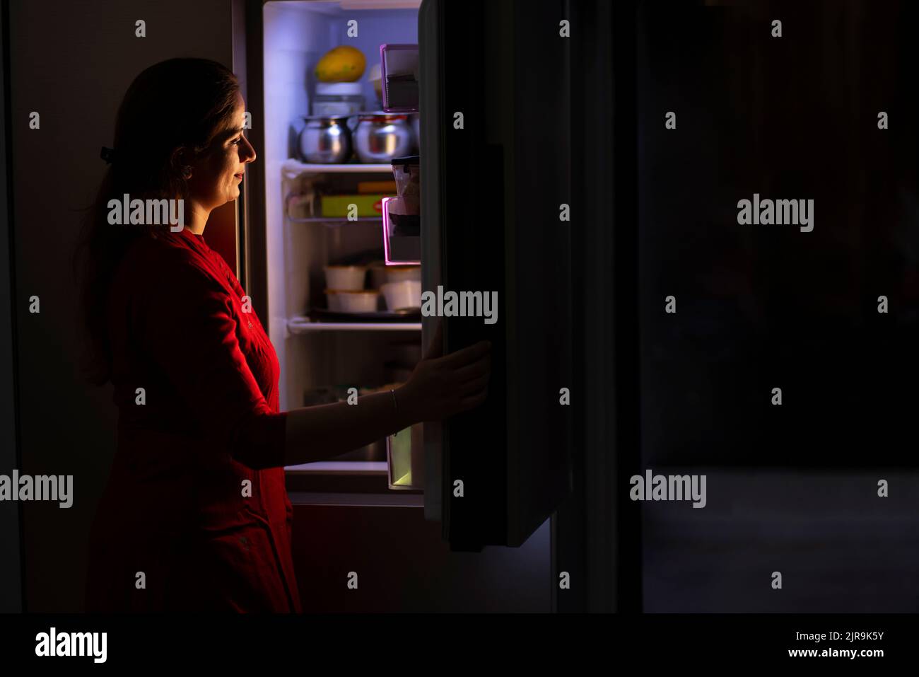 Giovane donna che guarda all'interno del frigorifero in cucina Foto Stock