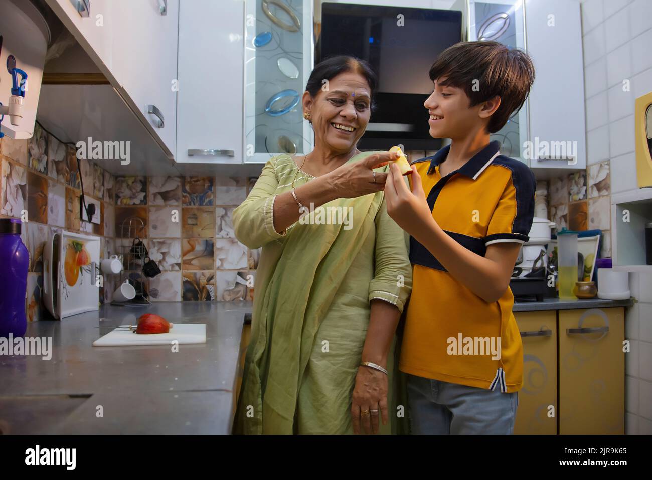 Donna anziana che dà un pezzo di mela al suo nipote in cucina Foto Stock