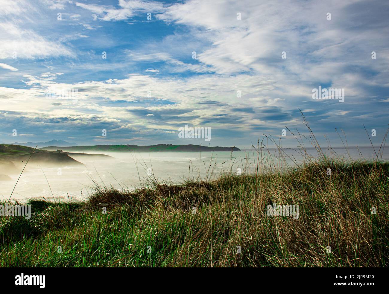 Paesaggio della costa del Mar Cantabrico nella città di Comillas in Cantabria (Spagna), dove si può vedere la nebbia marina e cielo nuvoloso Foto Stock