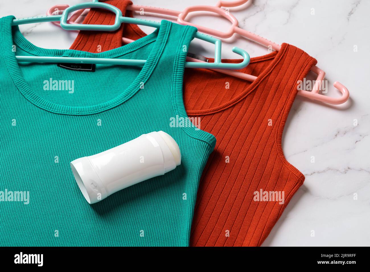 Deodorante solido su tettarella e canotta rossa su fondo in marmo. Appendiabiti antitraspirante su una canotta in Jersey di lino su grucce. Cura del corpo, cura della pelle. Foto Stock