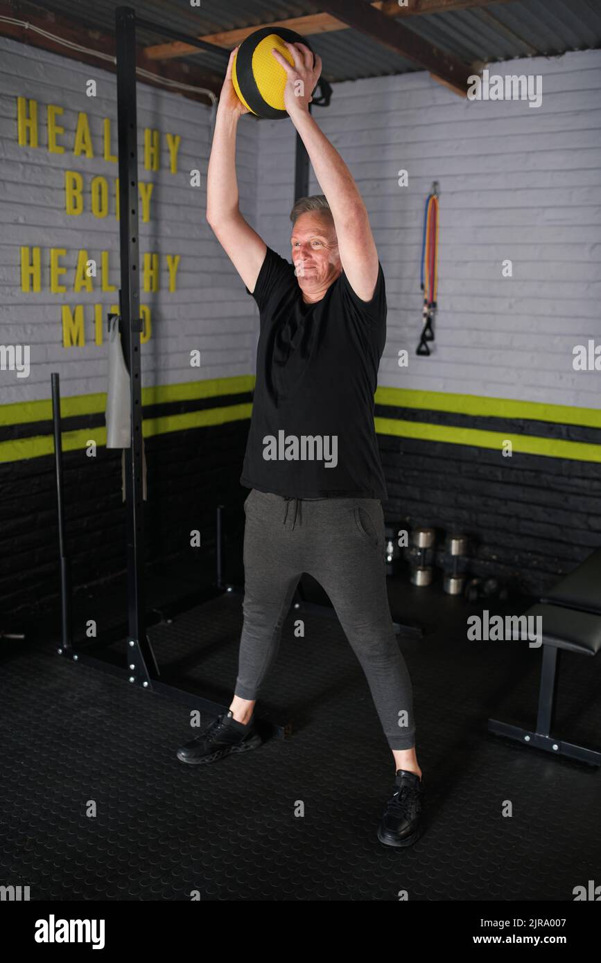 Uomo maturo che esercita in palestra domestica del garage. L'uomo anziano che fa la sfera ponderata della medicina smashes l'esercitazione. Foto Stock