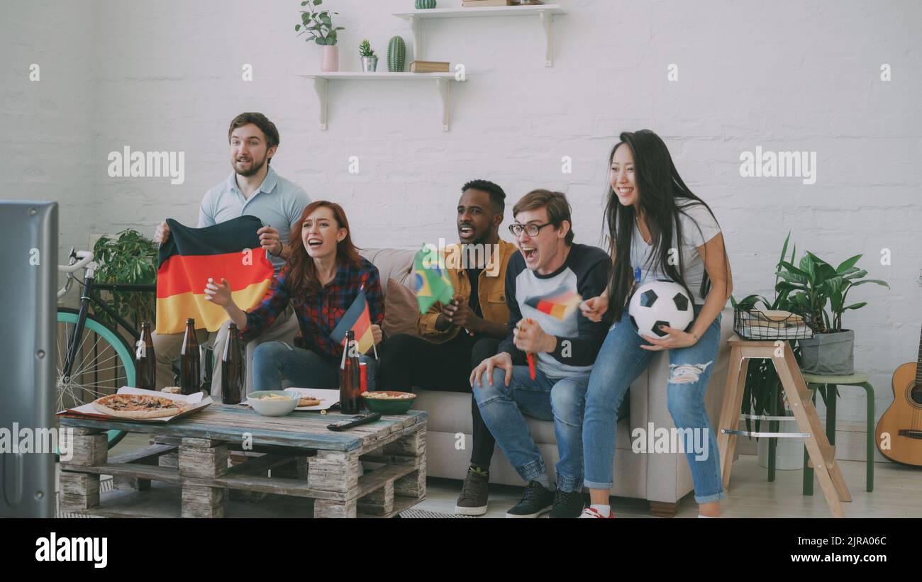 I giovani amici internazionali si allenano in TV insieme a casa. La maggior parte di loro sono contenti della vittoria della squadra tedesca, ma l'uomo brasiliano è rimasto deluso Foto Stock