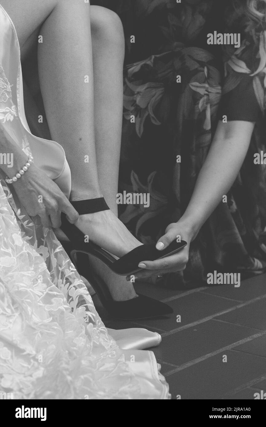 Una foto in scala di grigi di una mano che aiuta la sposa in abito bianco per indossare le scarpe nere Foto Stock