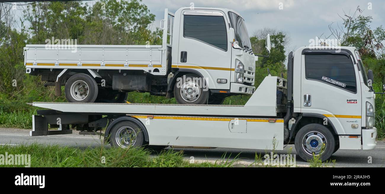 Un piccolo camion bianco che viene trasportato su un camion di traino più grande ma simile, preso in Thailandia. Foto Stock