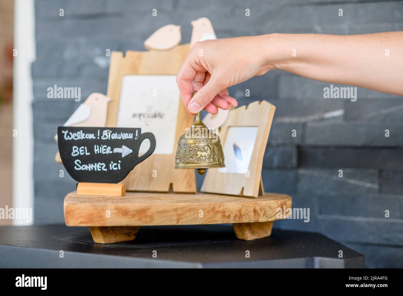 Suonando a mano una piccola campana posta accanto ad un cartello di benvenuto in più lingue, creando un'atmosfera calda e invitante. Foto Stock