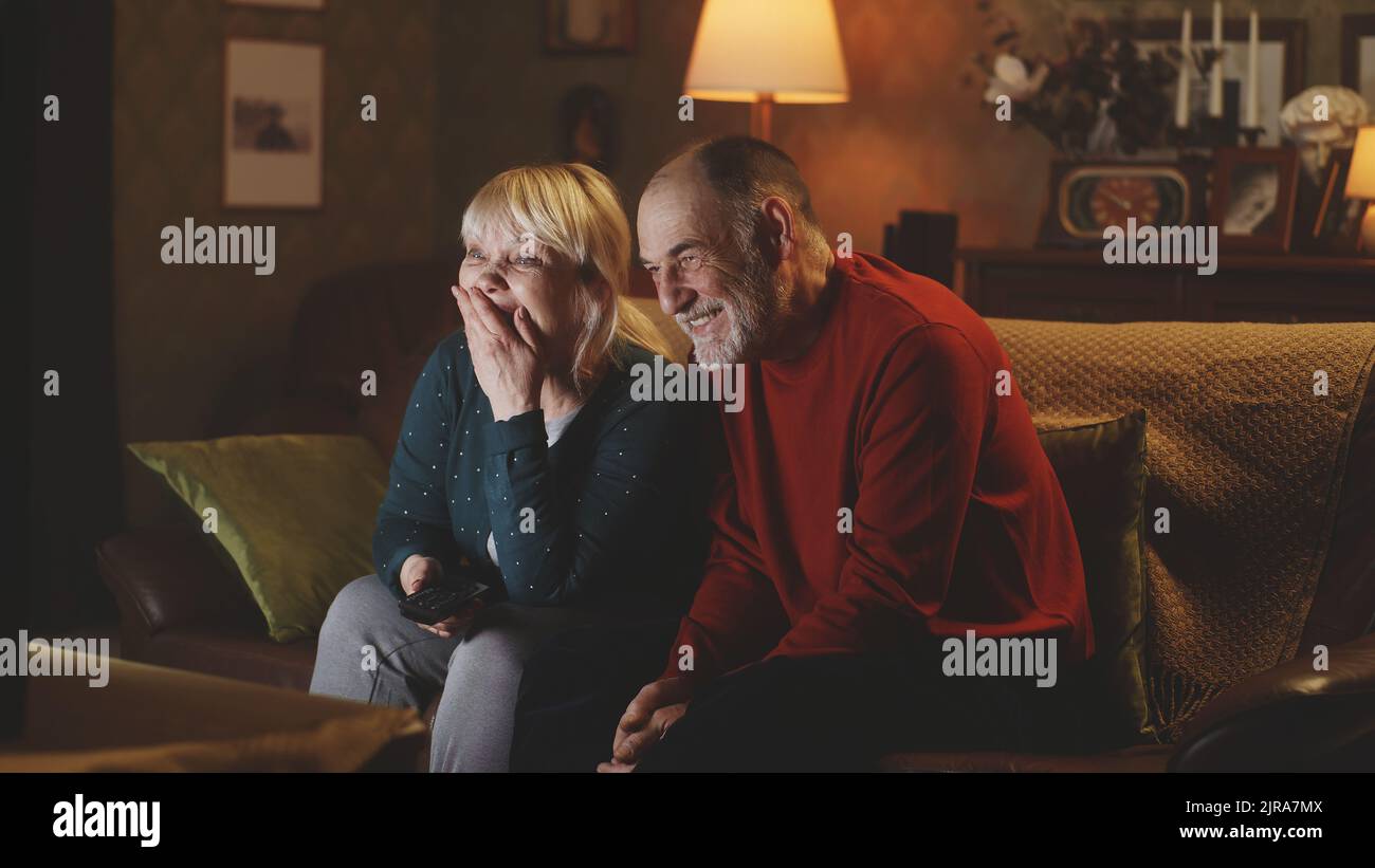 Felice marito e moglie senior ridendo di scherzo divertente mentre si siede sul divano e guardare la commedia in TV la notte a casa Foto Stock