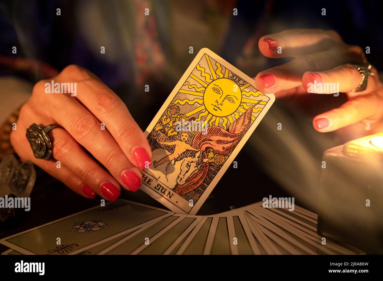 Fortune Teller mani femminili che mostrano la carta del tarocco del Sole, simbolo di positività e ottimismo, durante una lettura. Primo piano con luce a candela e fumo Foto Stock