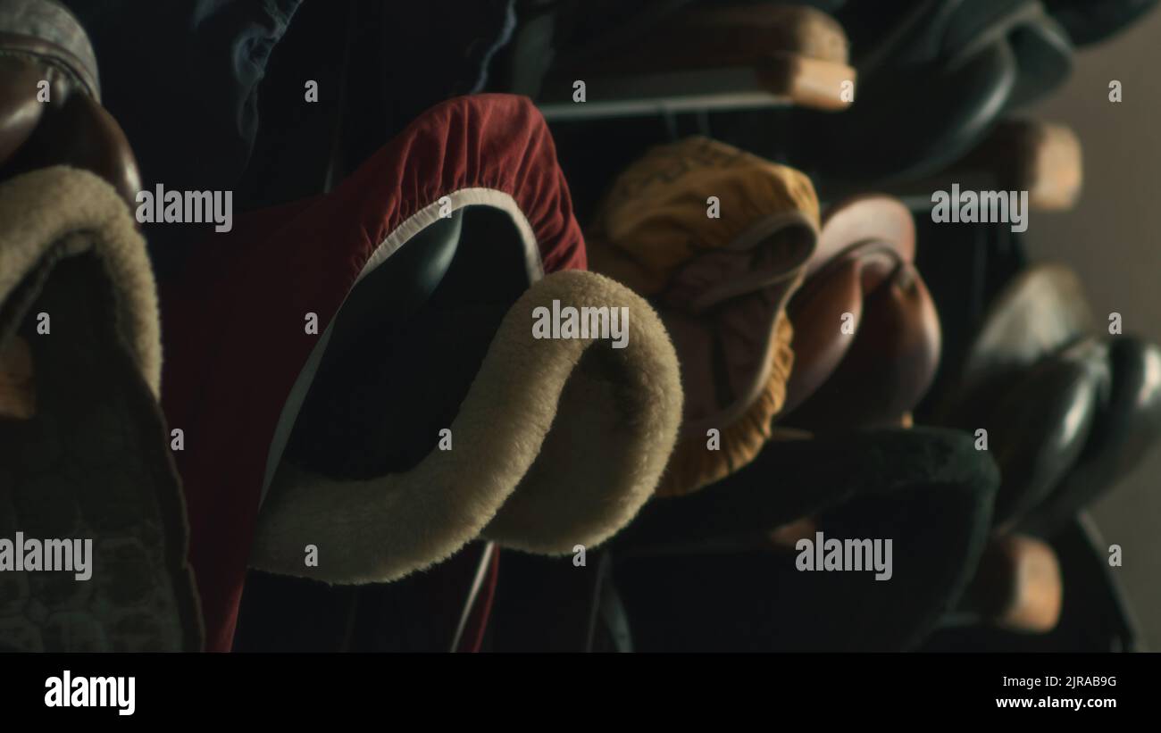 Varie selle a cavallo appese sulla cremagliera sul muro di stalla fioca in fattoria Foto Stock