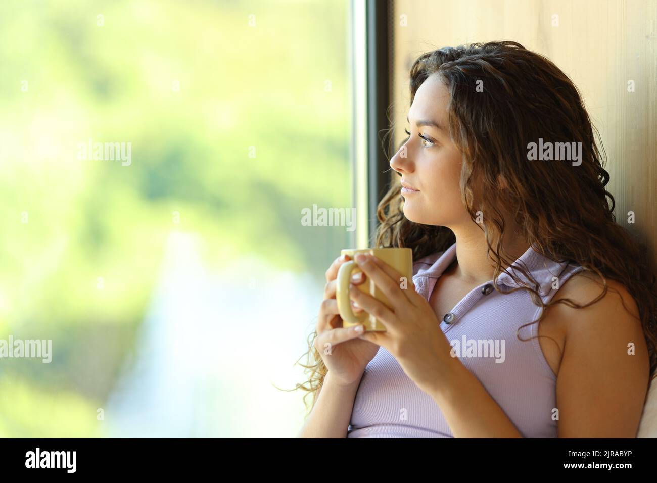 Bella donna rilassante bere caffè guardando attraverso una finestra in una stanza Foto Stock