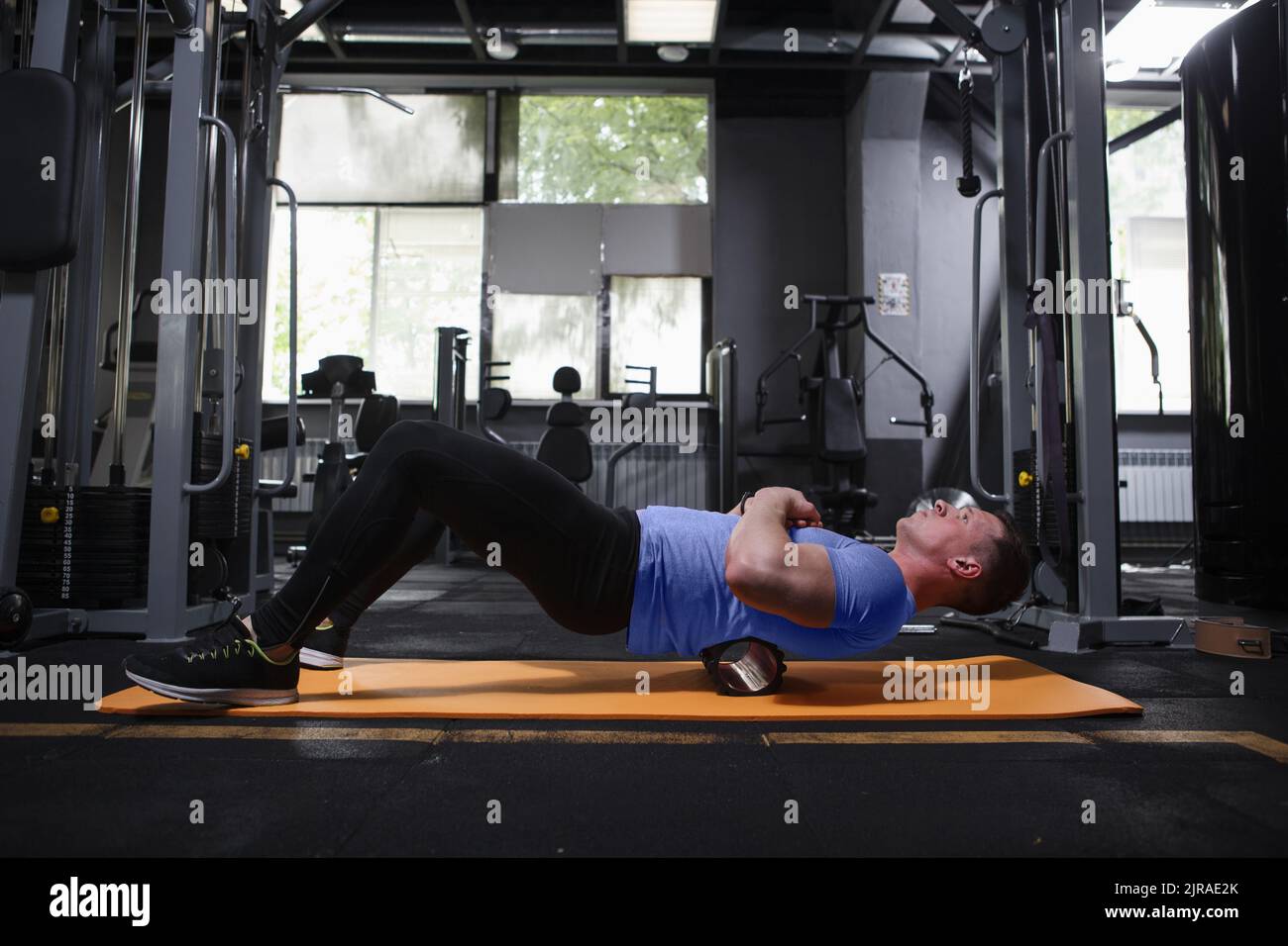 Scatto completo di un uomo di fitness che si rilassa dopo l'allenamento, usando il rullo di schiuma sui muscoli della schiena Foto Stock