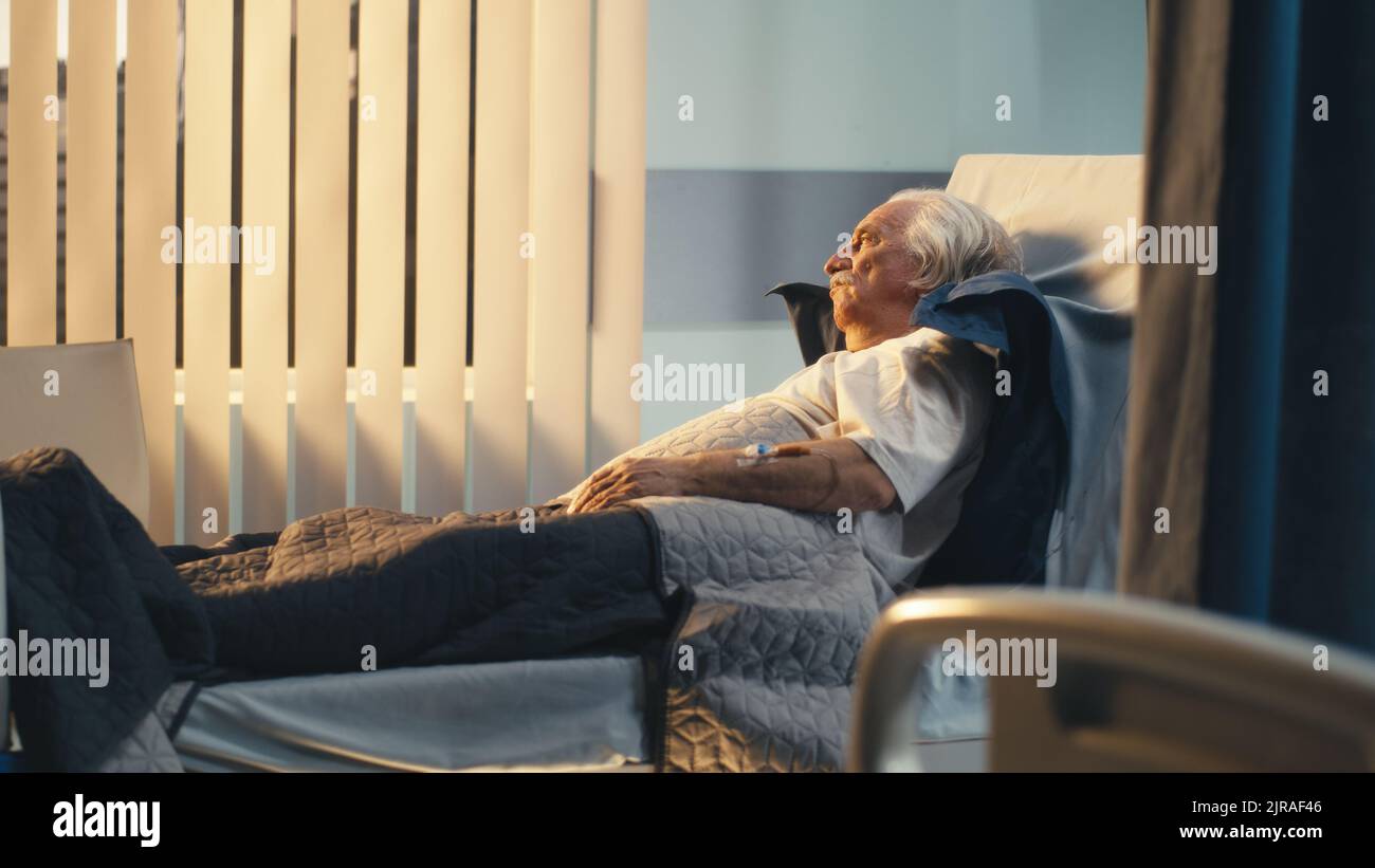 Vista panoramica a sinistra dell'uomo anziano solitario sdraiato sul letto e guardando lontano nel reparto della clinica moderna Foto Stock