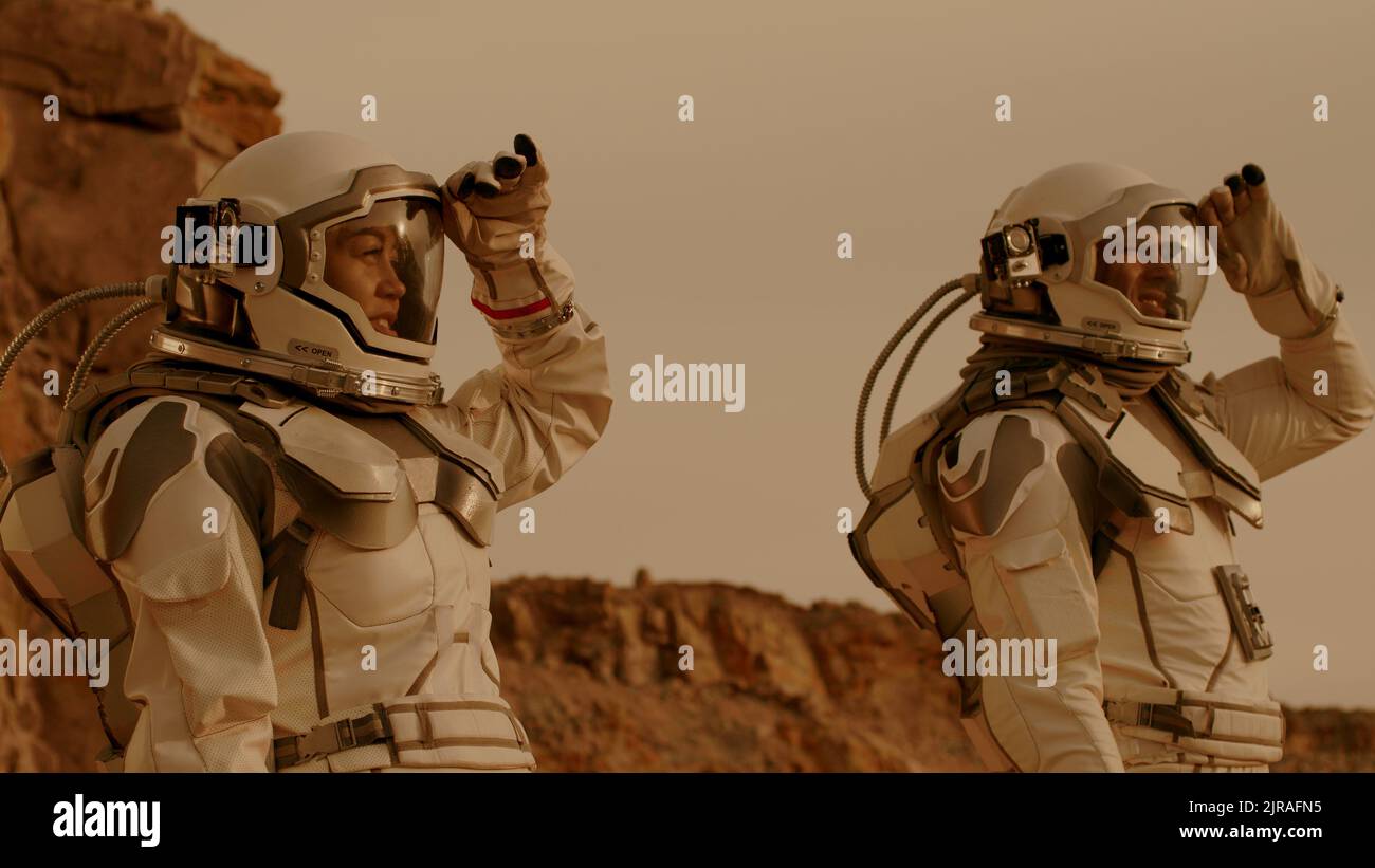 Uomo e donna negli spazi che toccano i caschi e si guardano intorno mentre esplorano Marte durante la missione di colonizzazione Foto Stock