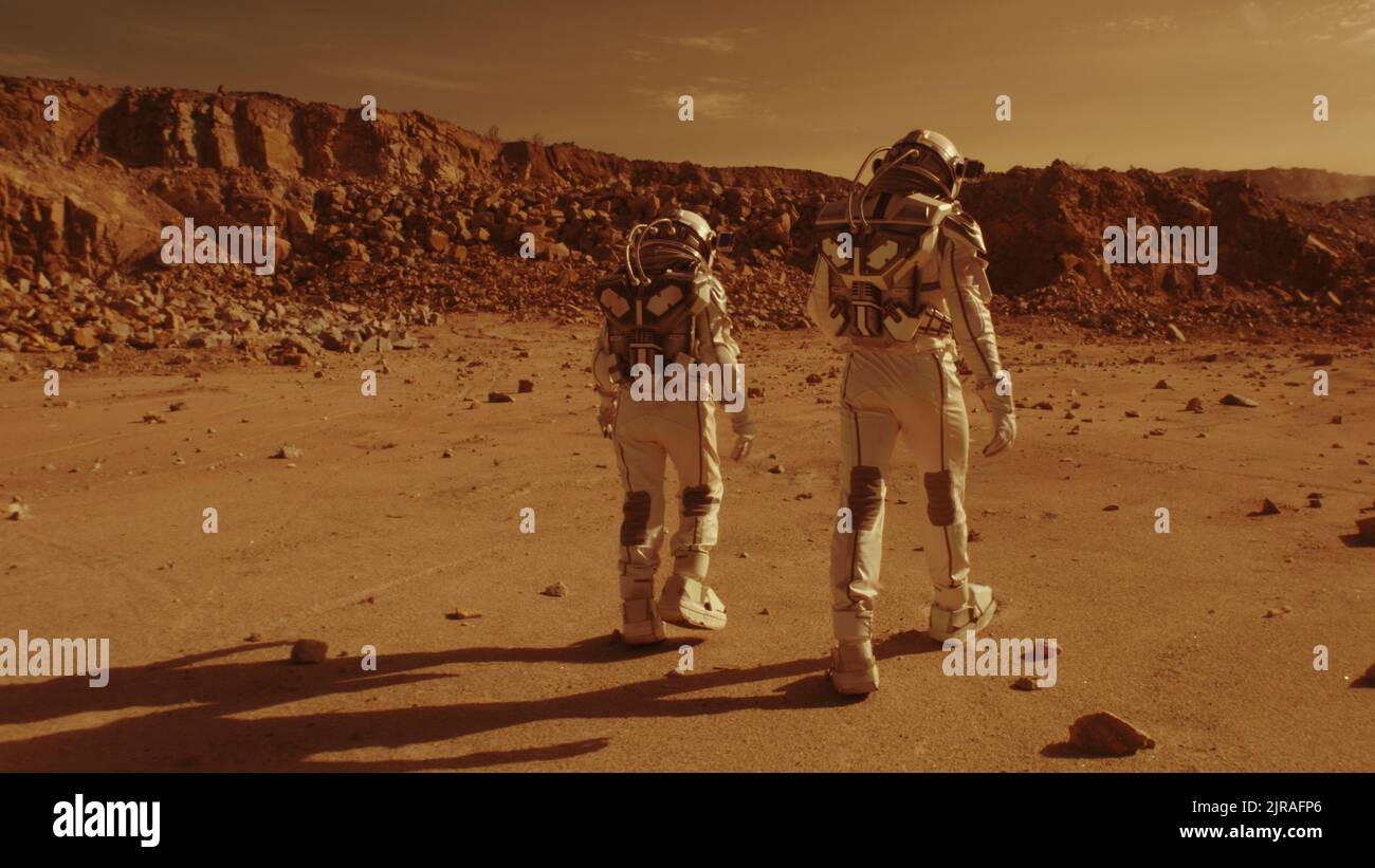 Tracking shot di persone anonime in spacesuit camminare su terreno arido insieme durante la colonizzazione di Marte Foto Stock